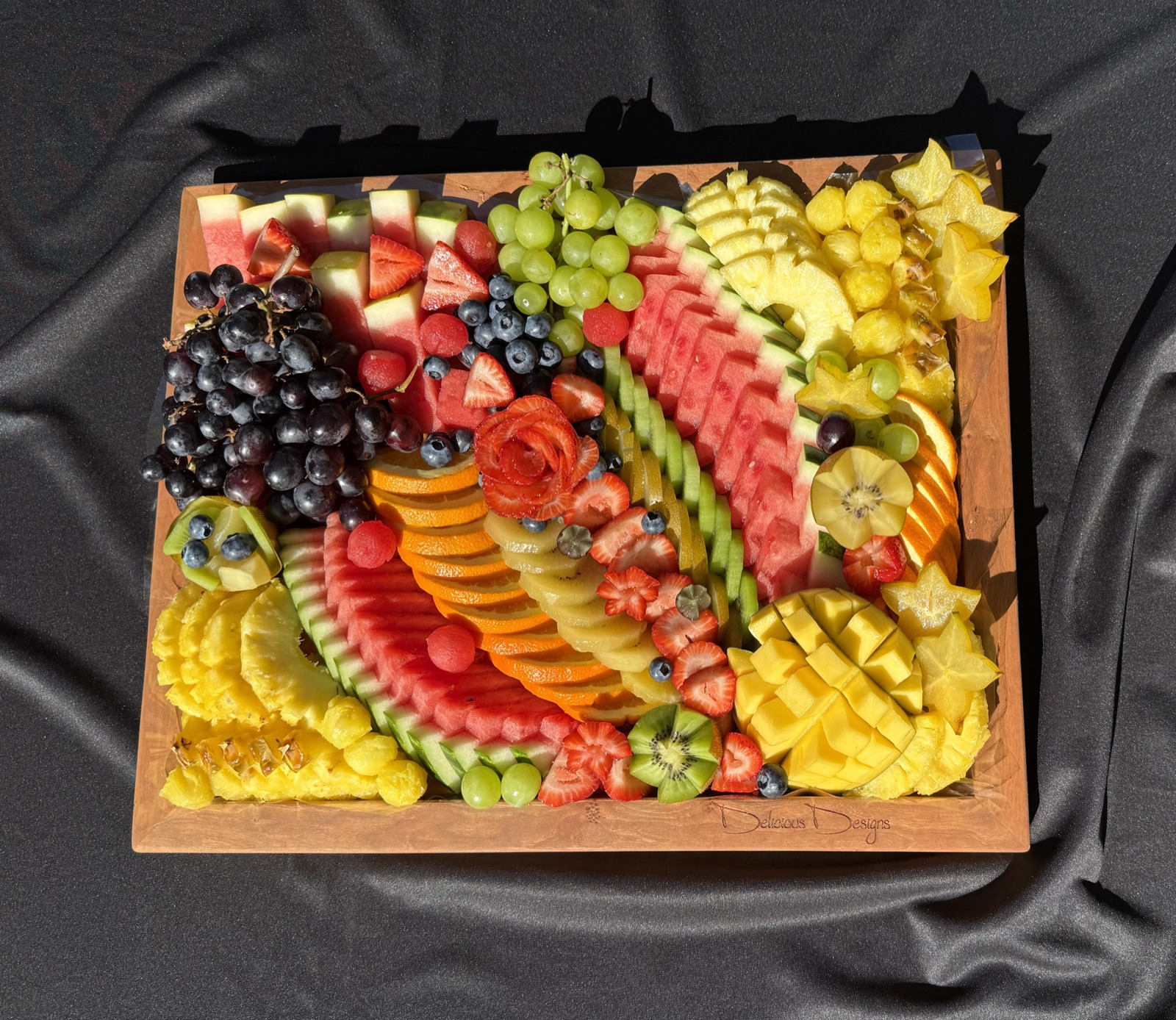 Medium fruit platter on a wooden board with watermelon, grapes, pineapple, mango and a carved watermelon rose