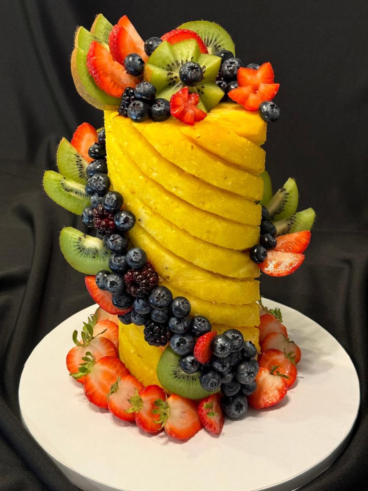 Double twist pineapple cake decorated with kiwi, strawberries, blueberries and blackberries